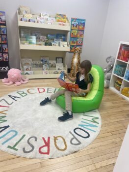 Ashleigh reads in a comfortable chair with bookshelves behind her. 