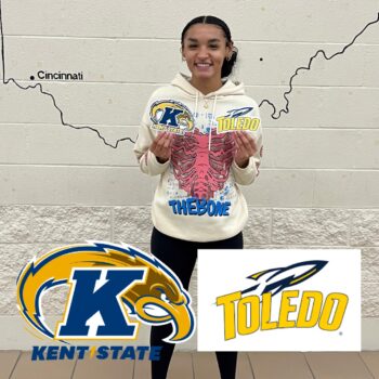 A TRIO participant, a black teenager with a smile, earrings, a hoodie and curly hair pulled back in a pony tail holds the logos of Kent State and the University of Toledo. after her acceptance.