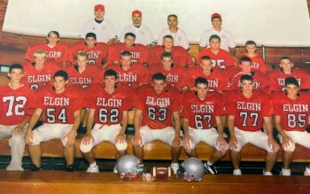 A football team poses in red Elgin jerseys with their coaches in the last row. 