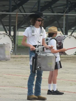Dylan wears a black cowboy hat, white T-shirt, jeans and brownwn boots while practicing drums.