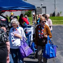 Seniors visit vendors and carry grocery bags with items from giveawways