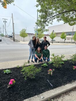 Five young women, Cummins employees, smile in front of a flower bled in downtown Marion. 