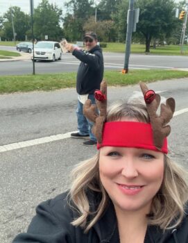 Jodi wears antlers while a volunteer stands behind her to collect donations. 