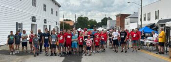 Runners, walkers, and volunteers fill the street. Many wear race numbers. Funds raised support the fight against Duchenne muscular dystrophy.