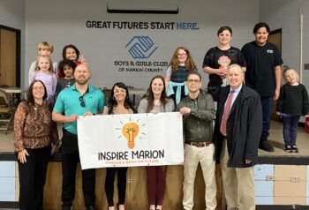 A group from Inspire Marion and the Boys & Girls Club, including kids, hold an banner with the Inspire Marion logo. Boys & Girls Club logo is in the background.