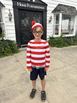 Luke, a boy with Duchenne muscular dystrophy, wears a 'Where's Waldo?" costume with a red and white striped hat, shirt, and black, round glasses.