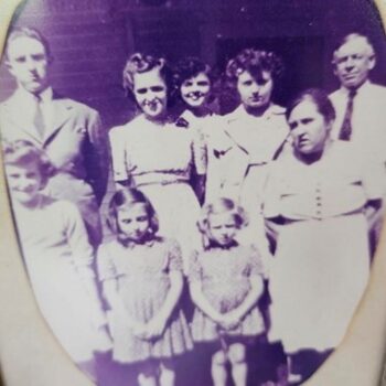 Two parents and their seven children from small girls to adults pose in this black-and-white photo. 