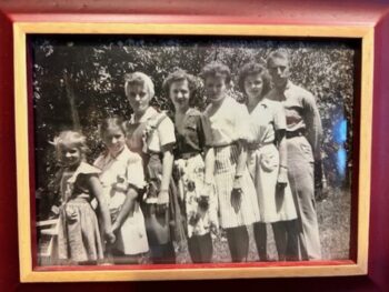 A black-and-white photo of the Overall sisters and their brother as children and teens. They stand from youngest to oldest. 