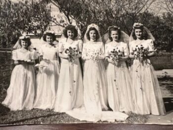 The six Overall sisters wear long dresses and carry bouquets in a wedding. 