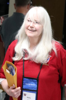 Aleta is a smiling white woman with long, white hair and bangs and a smile. 