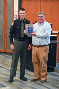 A young man in uniform smiles while the instructor hands him a plaque.