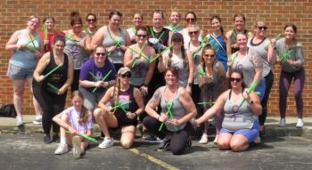 A group smiles while posing with drumsticks in a parking lot.