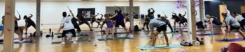 A group of men, women, and children exercise on mats while holding drum sticks.