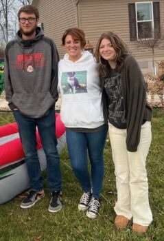 A smiling mother stands between her young adult son and a teenage daughter.