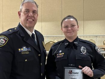 A young woman in uniform poses while holding the award next to the police chief, a tall man in uniform with gray hair. 