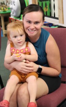 A mom holds her toddler daughter with red hair while they wait for storytime at the Explore-It-Torium.