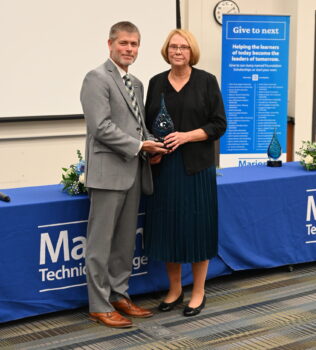 The present of the college presents Darlene with a tall blue glass award during her induction into the Alumni Hall of Fame. 