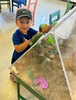 A boy smiles while reaching into a structure filled with sand and rocks at the Explore-It-Torium. 