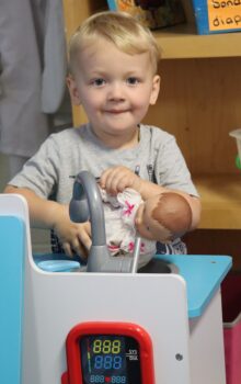 A small boy smiles while playing with a doll in a toy hospital at the Explore-It-Torium.  