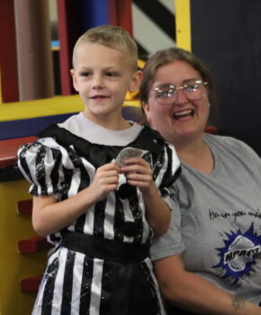 A boy playing dress-up holds a police sticker. He smiles next to his mother at story time at the Explore-It-Torium. 