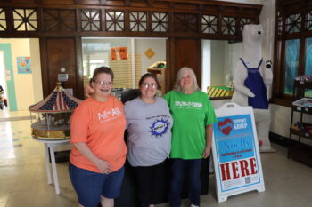 Thre women smile in the entrance of the museum. Two are long-time volunteers and one is the manager of theExplore-It-Torium. 