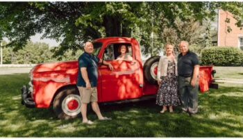 Two couples pose next to a red 1954 Ford truck under a tree. They founded Country Road Farms.