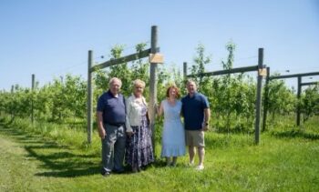 Two couples pose in front of young trees.