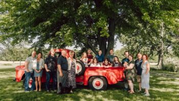 A large smiling family photo under a tree in front of the red 1954 Ford truck.