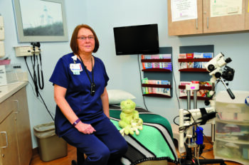 The nurse sits in teh exam room for survivors of sexual assault. There is a child's toy and various cameras and exam tools. 