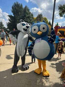 A giant gray Husky mascot and a large blue owl mascot pose. 