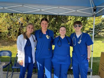 Students wear scrubs under a tent