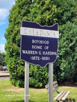 A black sign in the shape of the state of Ohio stating: Caledonia; Boyhood home of Warren G. Harding 1872- 1881.