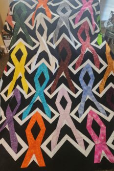 A black quilt covered with multi-colored quilted ribbons for different cancers.