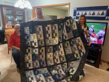 Family members hold a large quilt with a black and white block pattern.