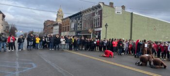 Onlookers watch as volunteers kneel on the ground to race their peanuts across the street.