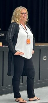 A blonde woman smiles while presenting. 