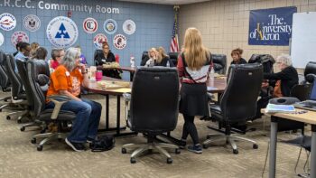 A group of women at a conference table listens to presenters. 