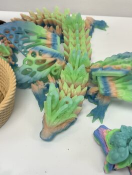 A close-up of a 3-D printed dragon in blue, peach and light green colors across the head, body, wings and tail.