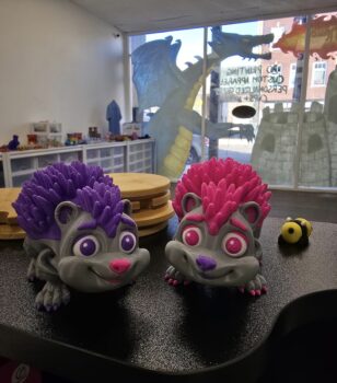 Two gray hedgehogs with colored spikes, eyes, noses, and toenails. One has purple spikes and the other has pink pink 