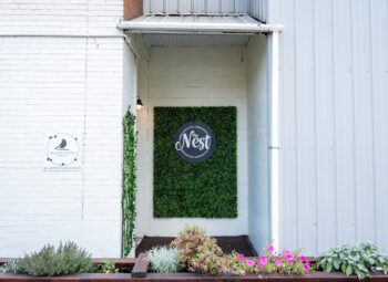 A white brick building with a small Yellow Finch sign and a green entryway with a green background and "The Nest" logo.