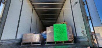 Boxes on pallets are filled to the doors of a trailer. A handmade sign lists the many local donors to the hurricane relief drive. 