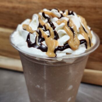 A tall chocolate drink with whipped cream and chocolate and peanut butter sauce on top.