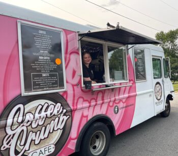 A worker smiles inside the food truck with a large pink logo and menu on its outside 