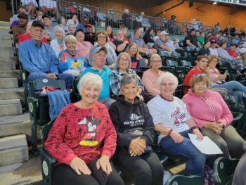 A group of seniors smile while sitting in the stands of a baseball game. 