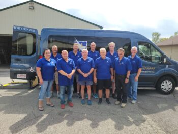 A woman and a group of drivers smile in front of a van.