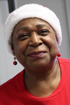 A black woman with a santa cap, a red shirt, red earrings smiles. 