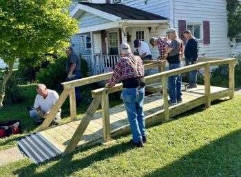 A group of seniors construct a ramp outside of a home.