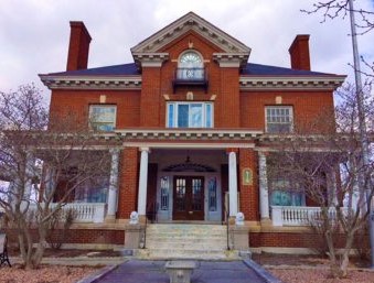 A three-story brick building. The wide front entrance has white pillars and a wrap-around porch. 