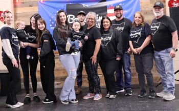 The owners, servers, and some of their children pose on a stage.