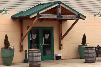 A tan and peach cement block building with a green awning and green barrels.